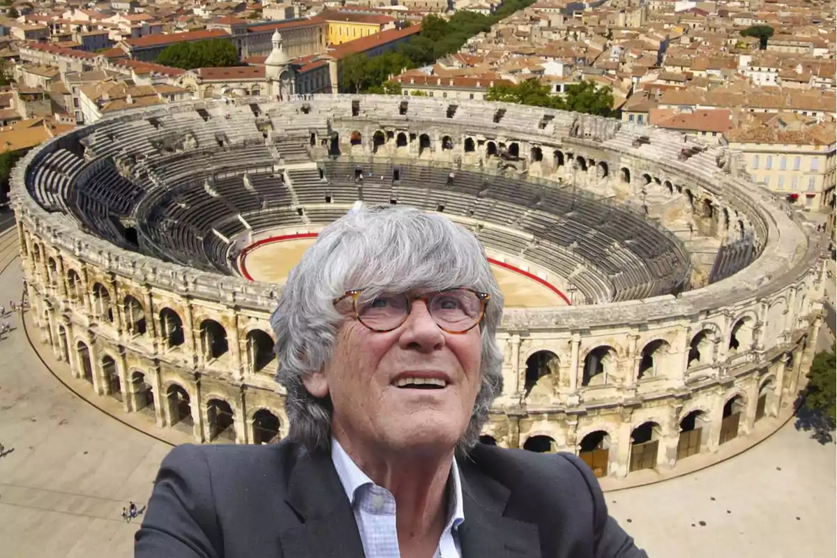 Hombre de cabello canoso y gafas frente a un anfiteatro romano antiguo rodeado de una ciudad