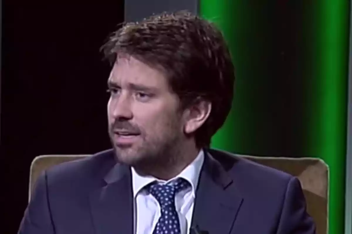 Un hombre con traje y corbata está sentado en un estudio de televisión con fondo verde. Un hombre con traje y corbata está sentado en un estudio de televisión con fondo verde.