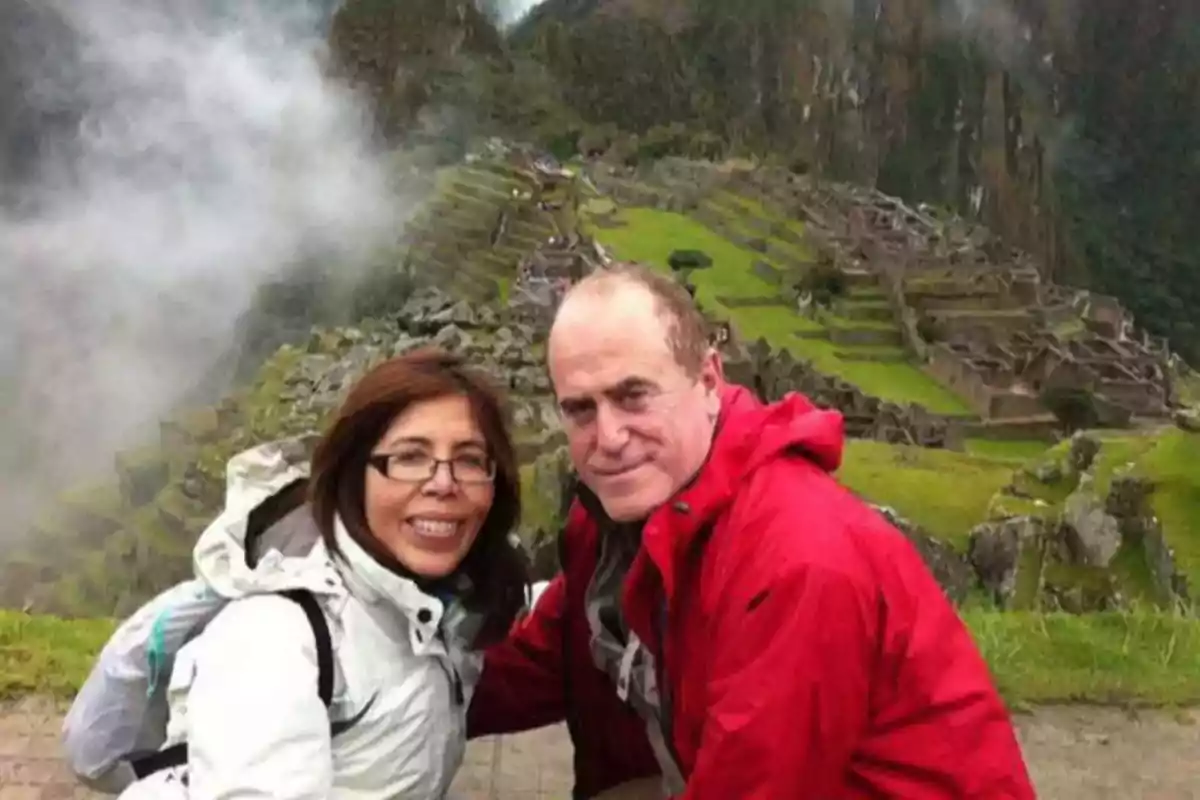 Una pareja sonríe mientras posa frente a las ruinas de Machu Picchu en un día nublado.