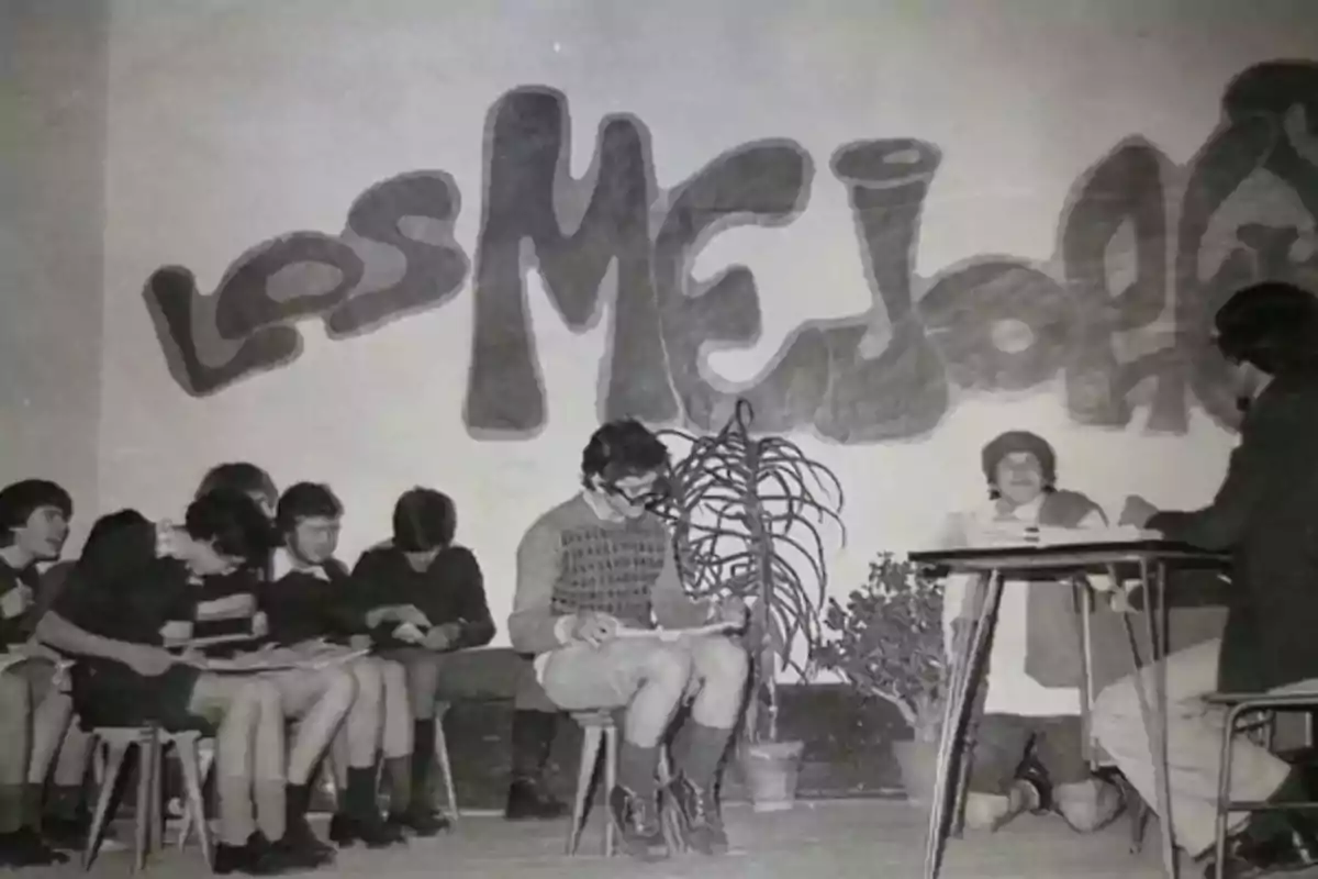 Un grupo de personas sentadas en sillas frente a un mural que dice 