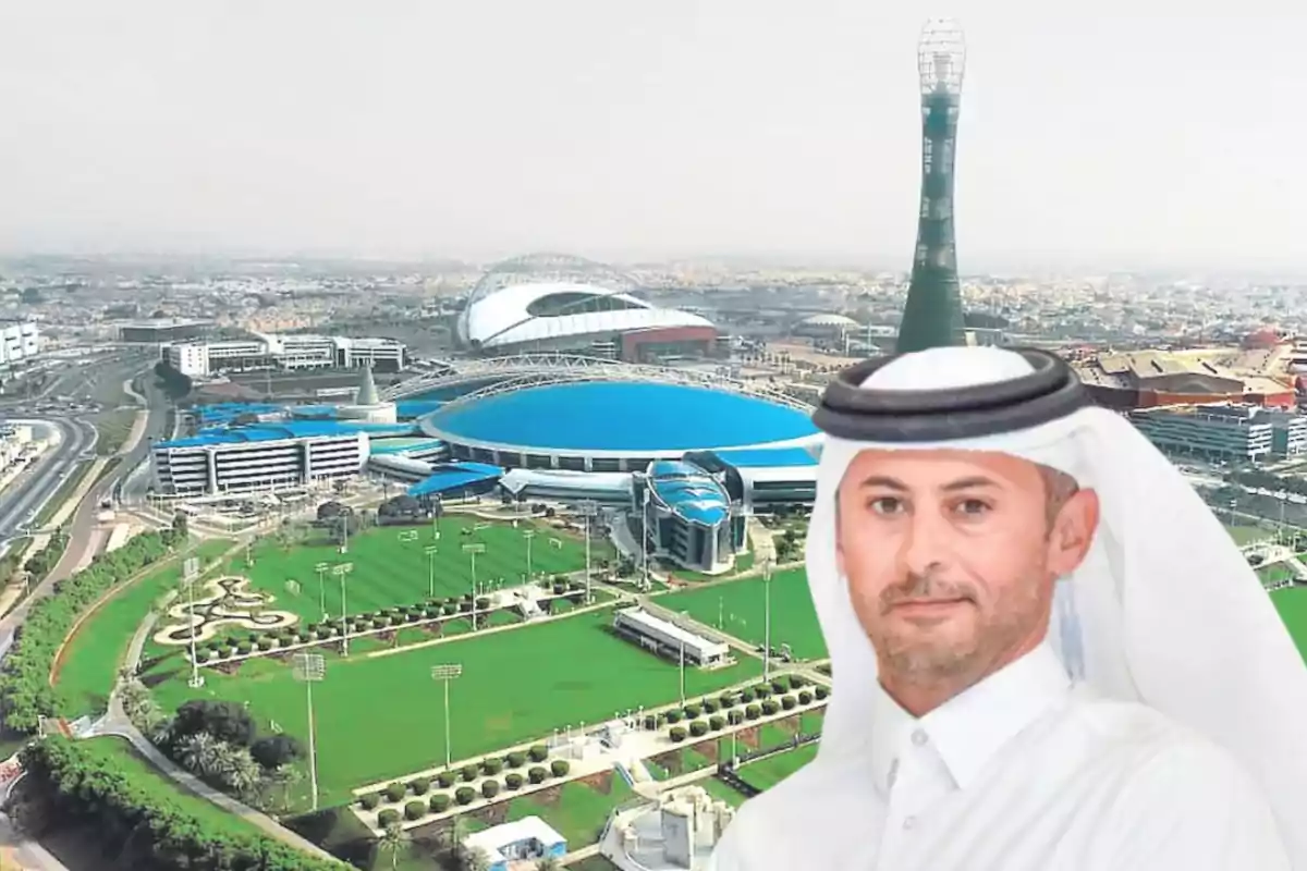Un hombre con vestimenta tradicional árabe aparece en primer plano frente a un complejo deportivo moderno con edificios y áreas verdes. Un hombre con vestimenta tradicional árabe aparece en primer plano frente a un complejo deportivo moderno con edificios y áreas verdes.