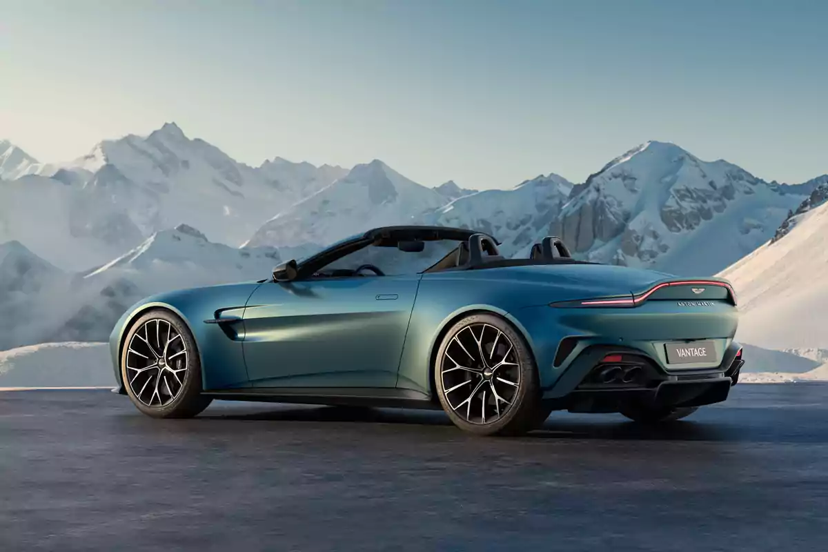 Un coche Aston Martin Vantage Roadster deportivo descapotable azul estacionado frente a un paisaje montañoso nevado.