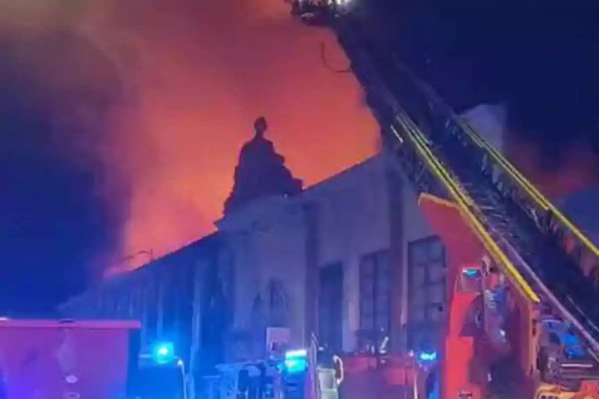 Un edificio en llamas durante la noche con bomberos y equipos de emergencia trabajando en el lugar.