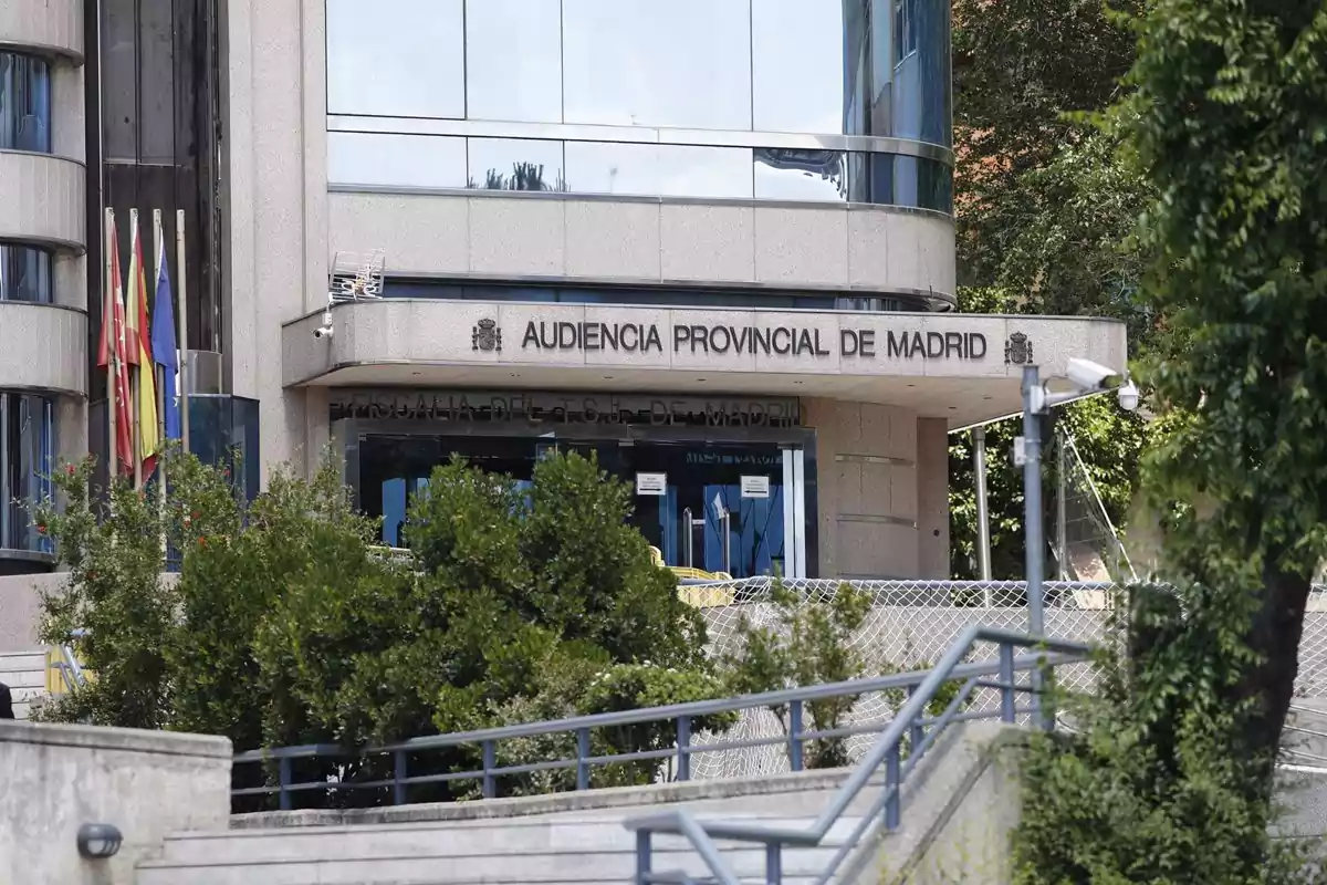 Edificio de la Audiencia Provincial de Madrid con banderas en la entrada y rodeado de vegetación.