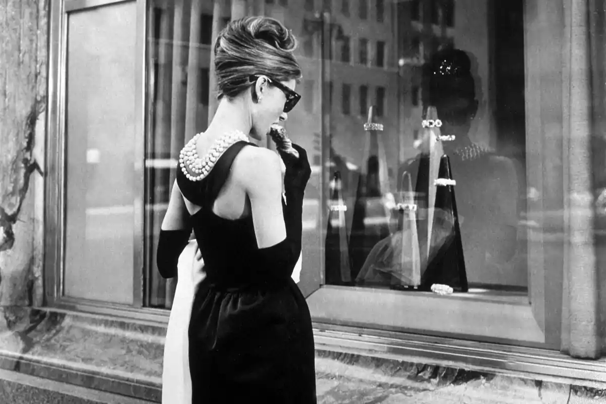 Una mujer elegante con gafas de sol y un vestido negro observa un escaparate de joyería.