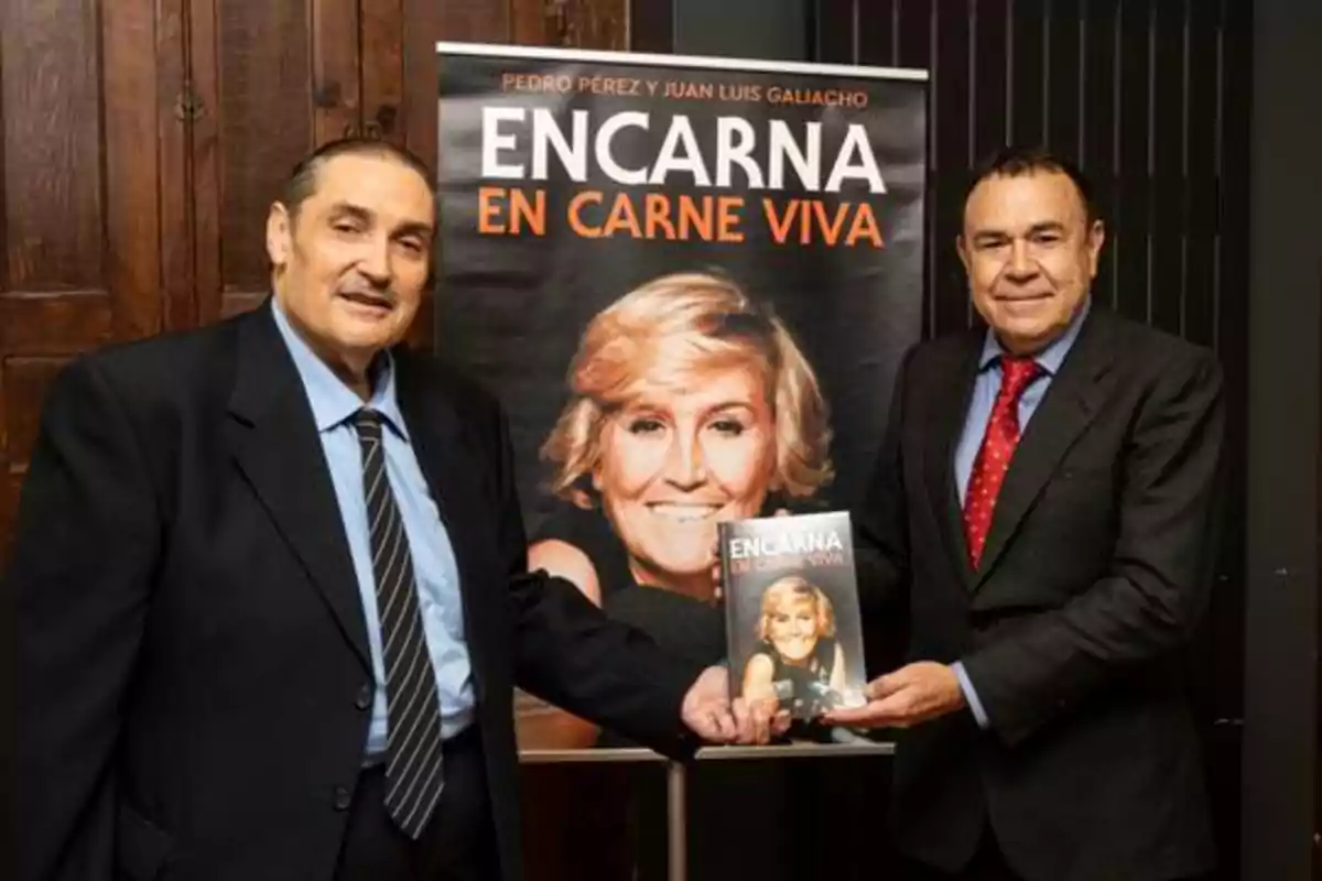 Dos hombres posan junto a un cartel y un libro titulado 