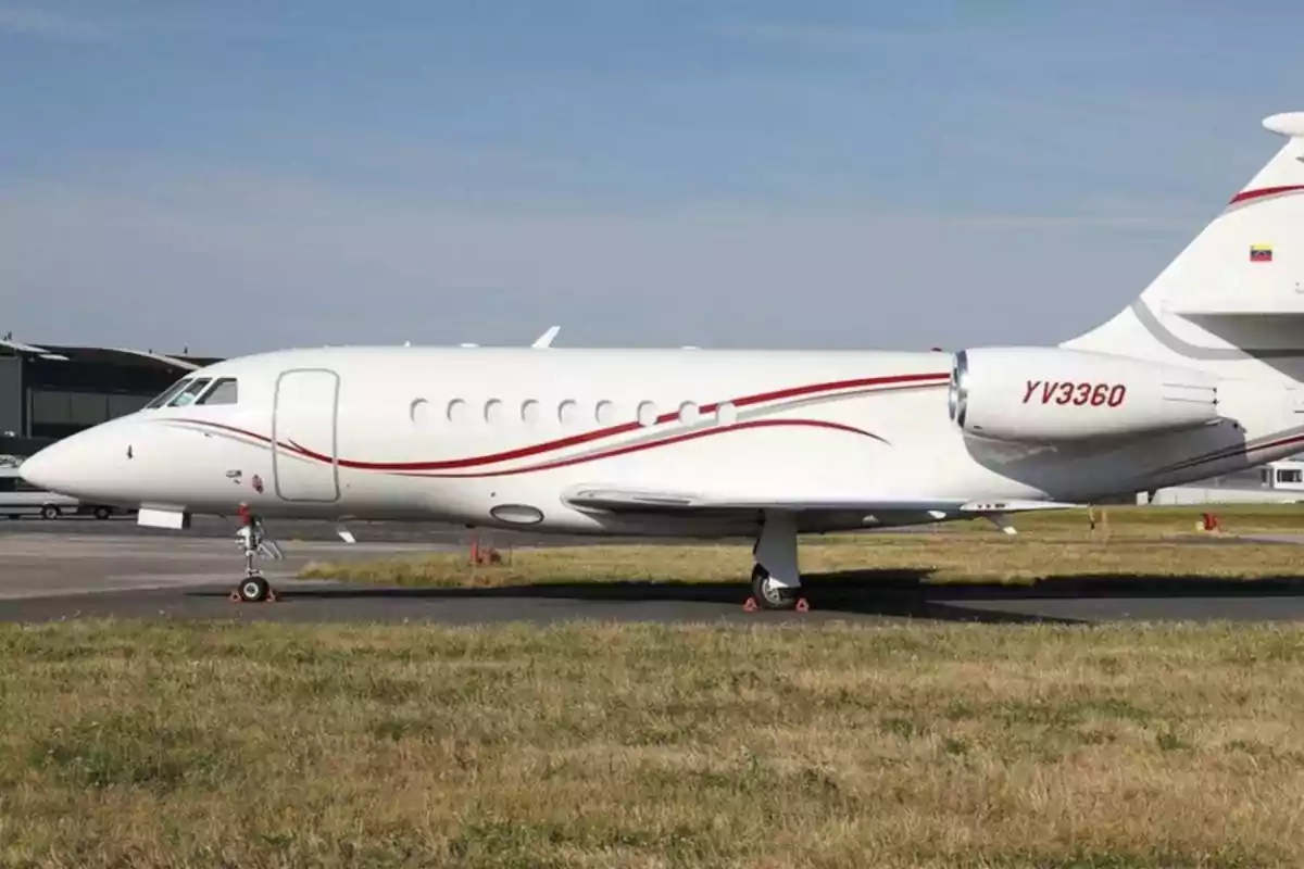 Un avión privado blanco con detalles rojos estacionado en una pista de aterrizaje.