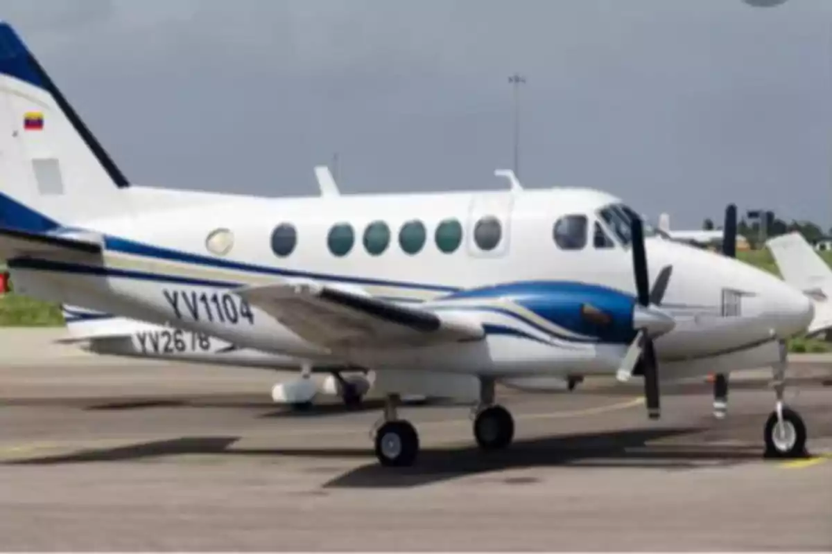 Avión bimotor blanco y azul estacionado en una pista de aeropuerto.