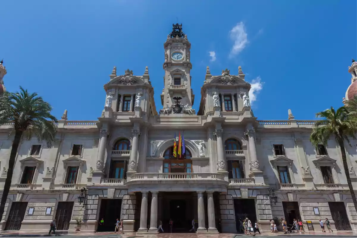 Fachada del Ayuntamiento de Valencia con cielo azul y personas paseando frente al edificio Fachada del Ayuntamiento de Valencia con cielo azul y personas paseando frente al edificio