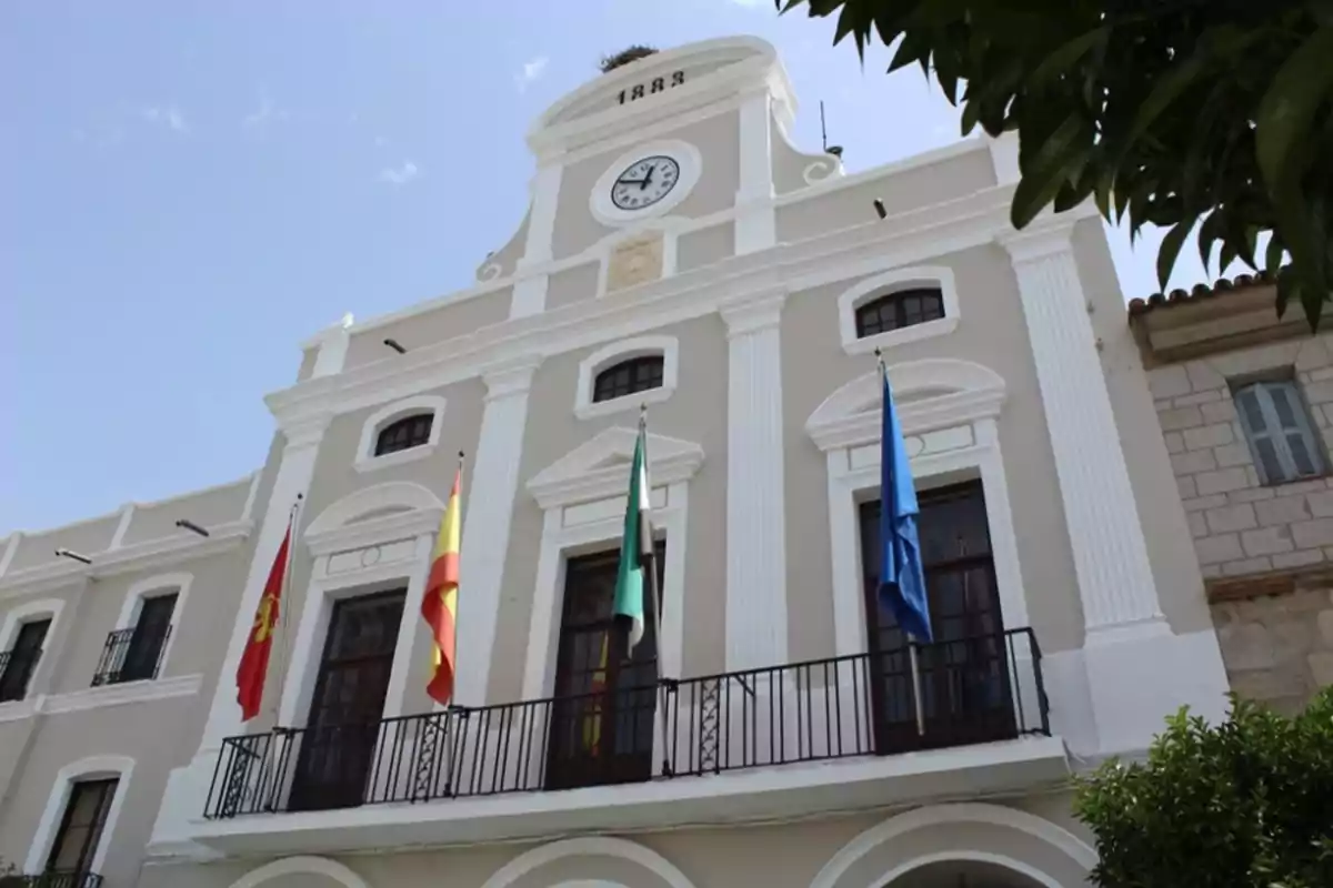 Fachada de un edificio histórico con un reloj en la parte superior y varias banderas en el balcón.