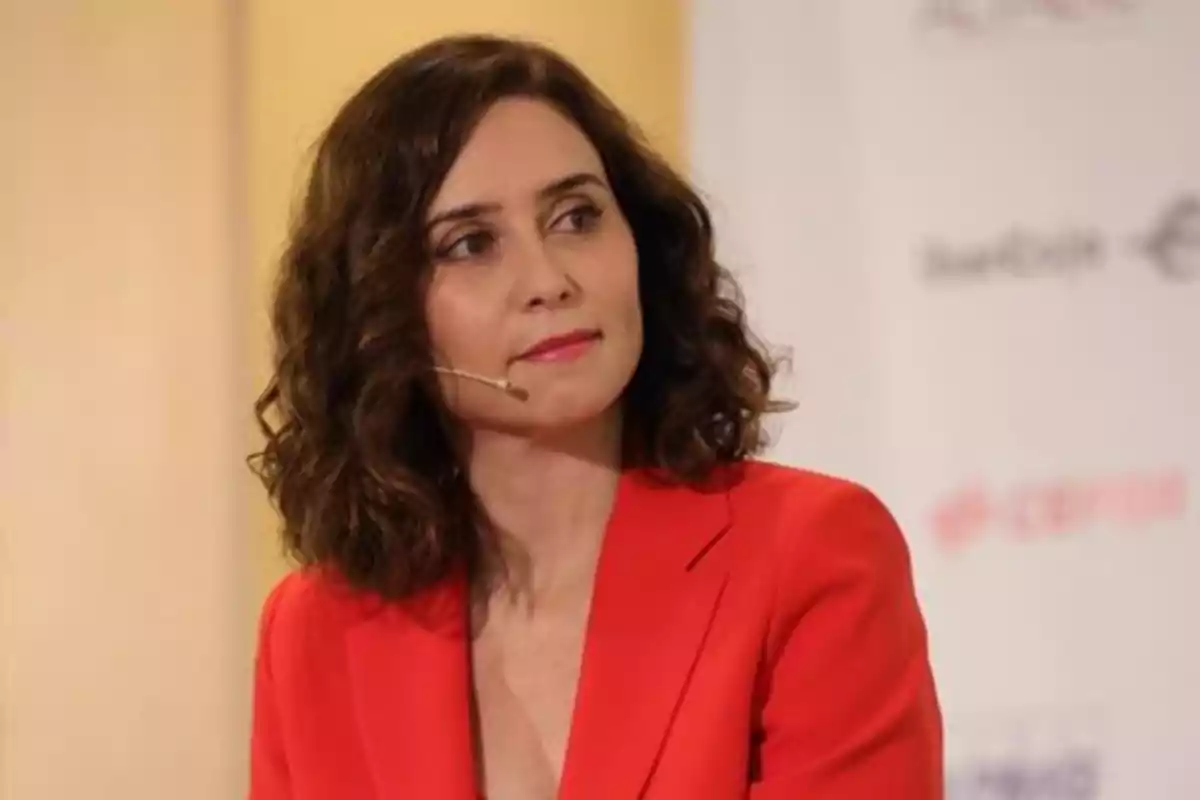 Una mujer con cabello rizado y un micrófono de diadema lleva un traje rojo y está en un evento. Una mujer con cabello rizado y un micrófono de diadema lleva un traje rojo y está en un evento.
