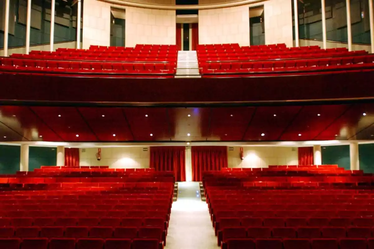 Auditorio vacío con asientos rojos y un escenario al fondo.