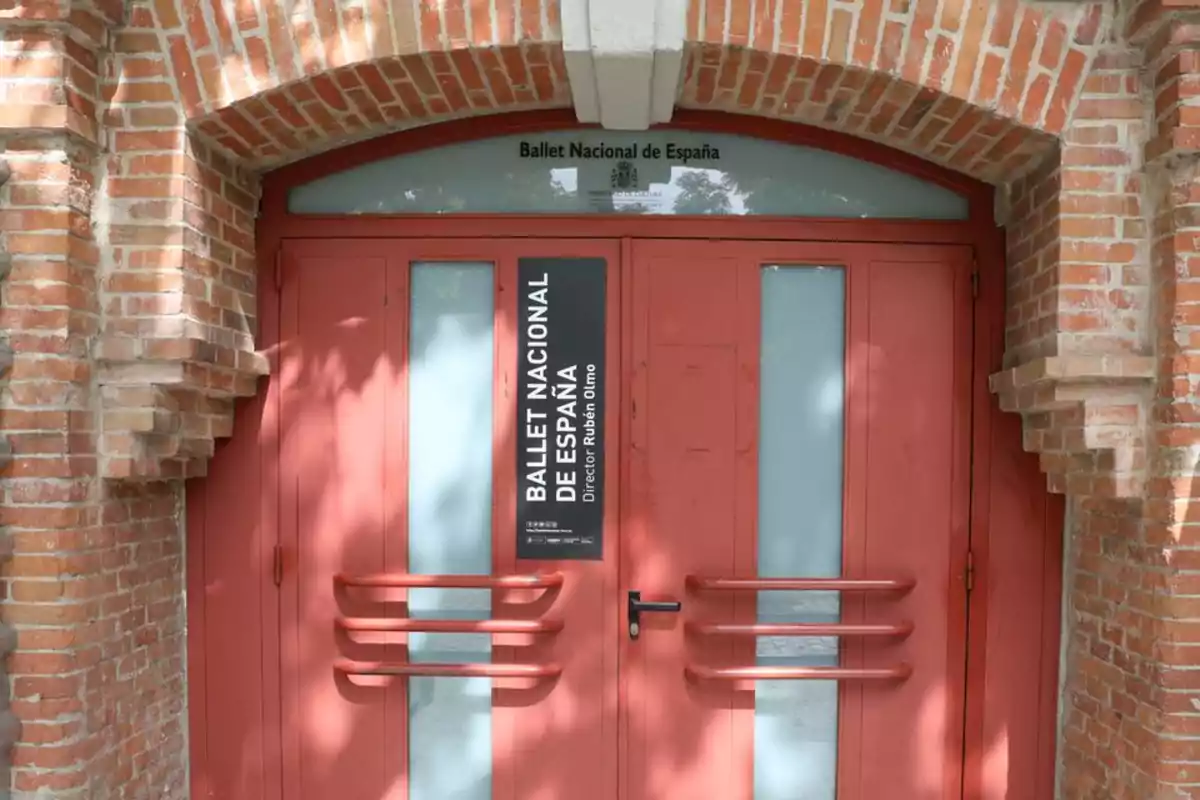 Puerta roja de entrada al Ballet Nacional de España con marco de ladrillo y letrero negro vertical