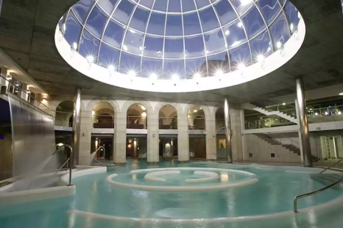 Piscina interior con techo de cúpula de vidrio y cascada de agua en un spa lujoso.