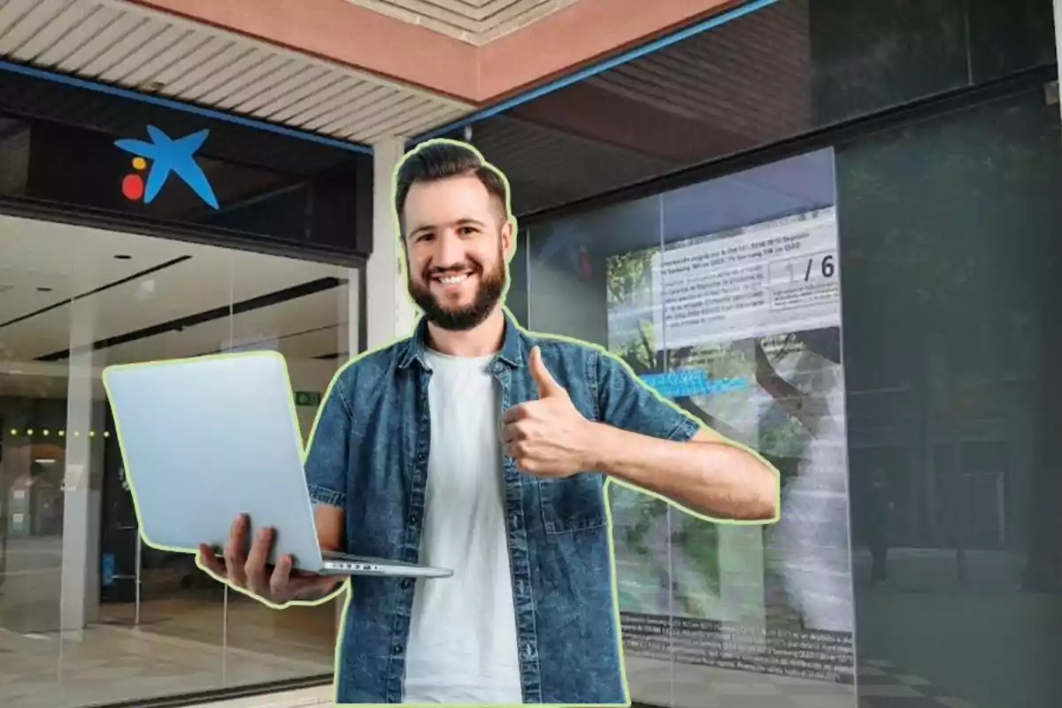 Un hombre sonriente con barba sostiene una computadora portátil y hace un gesto de aprobación con el pulgar hacia arriba, frente a un edificio con el logotipo de una entidad financiera.