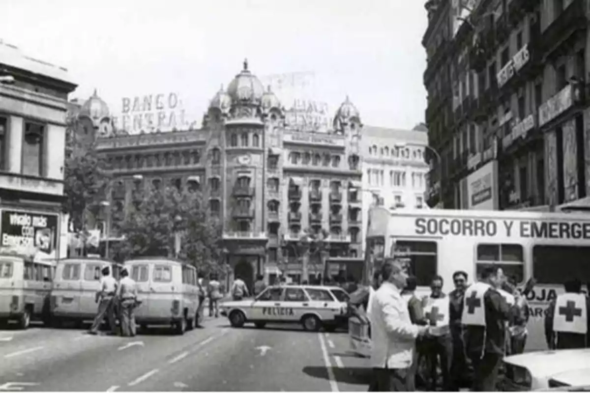 Escena urbana en blanco y negro con vehículos de emergencia y personal de la Cruz Roja frente a un edificio histórico con letrero de "Banco General".