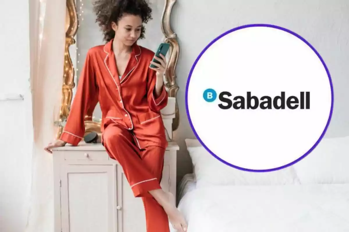 Una mujer en pijama rojo sentada en un mueble, mirando su teléfono, con el logo de Sabadell al lado.