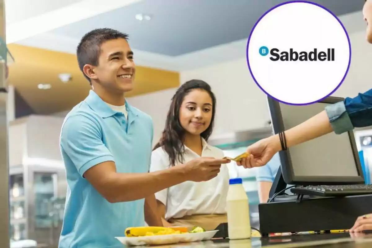 Un joven sonriendo mientras paga en una caja registradora con el logo de Sabadell en la esquina superior derecha.