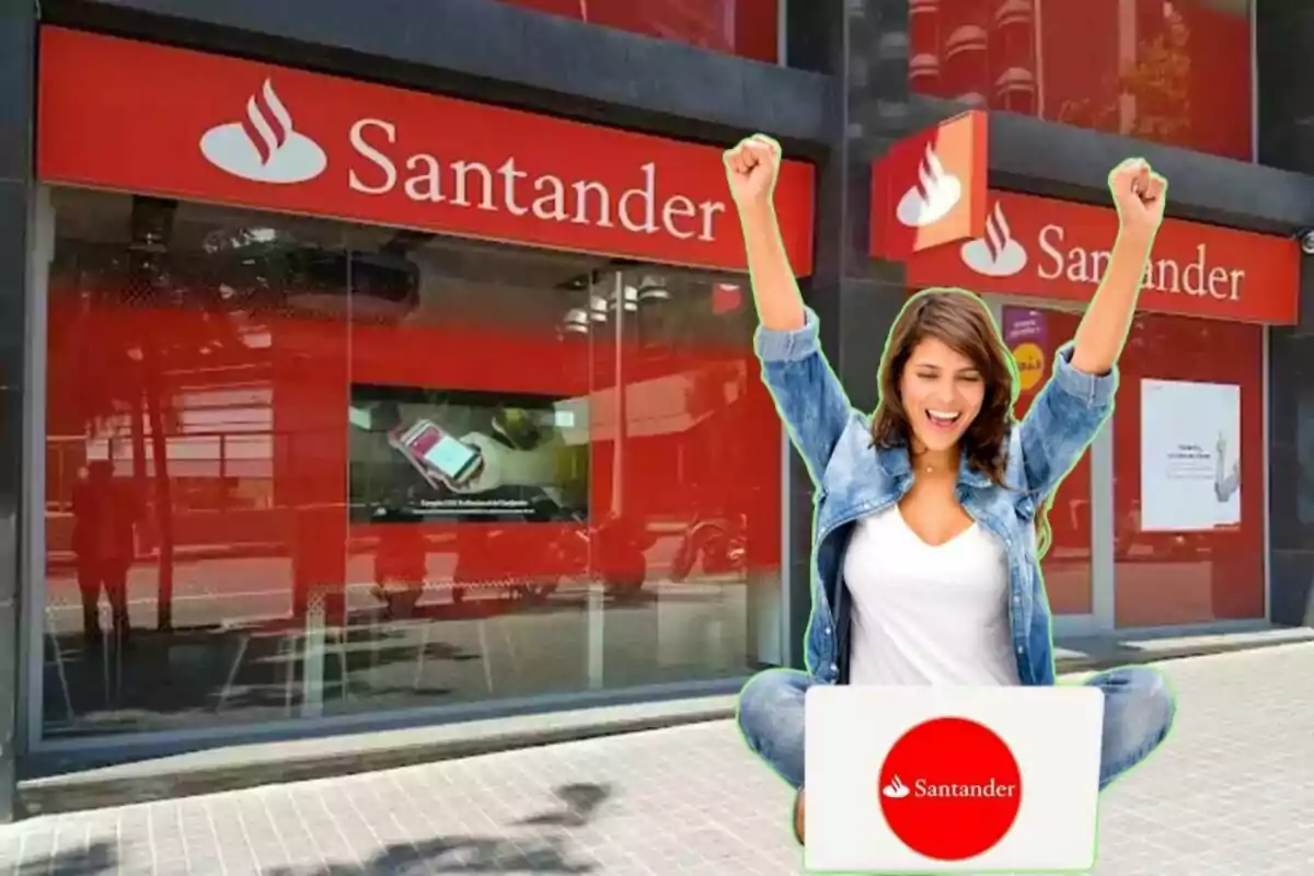 Mujer feliz con los brazos levantados frente a una sucursal del banco Santander con una computadora portátil.