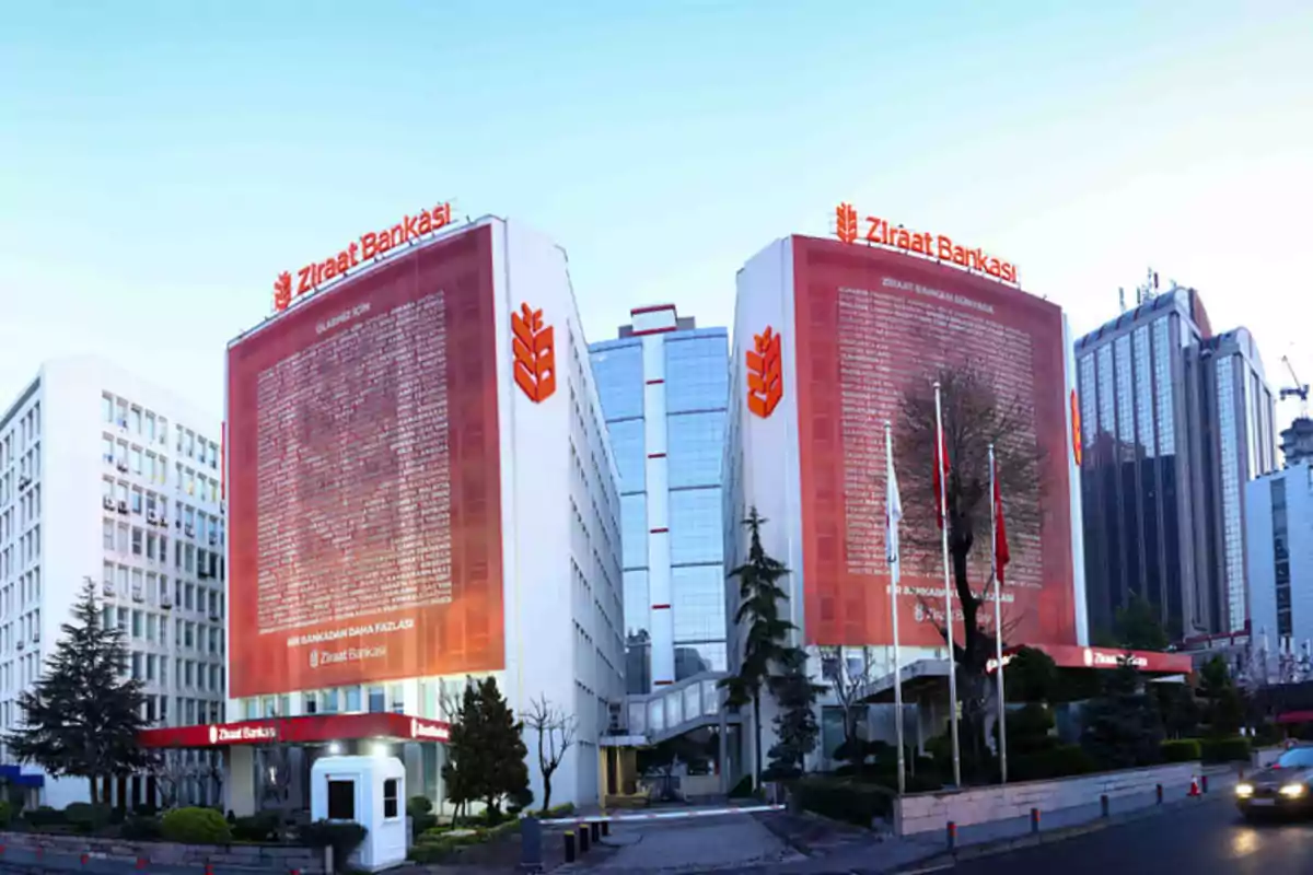 Edificios del banco Ziraat con letreros rojos y logotipos en una ciudad moderna.