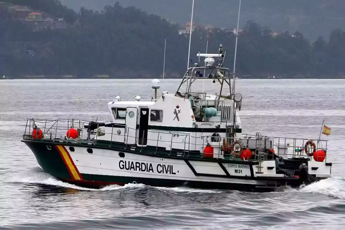 Barco de la Guardia Civil navegando en un cuerpo de agua con colinas boscosas al fondo.