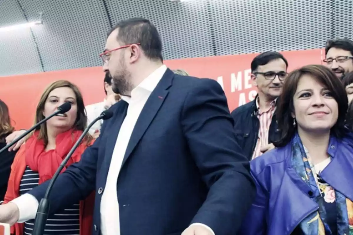 Grupo de personas en un evento público con micrófonos y fondo rojo Grupo de personas en un evento público con micrófonos y fondo rojo