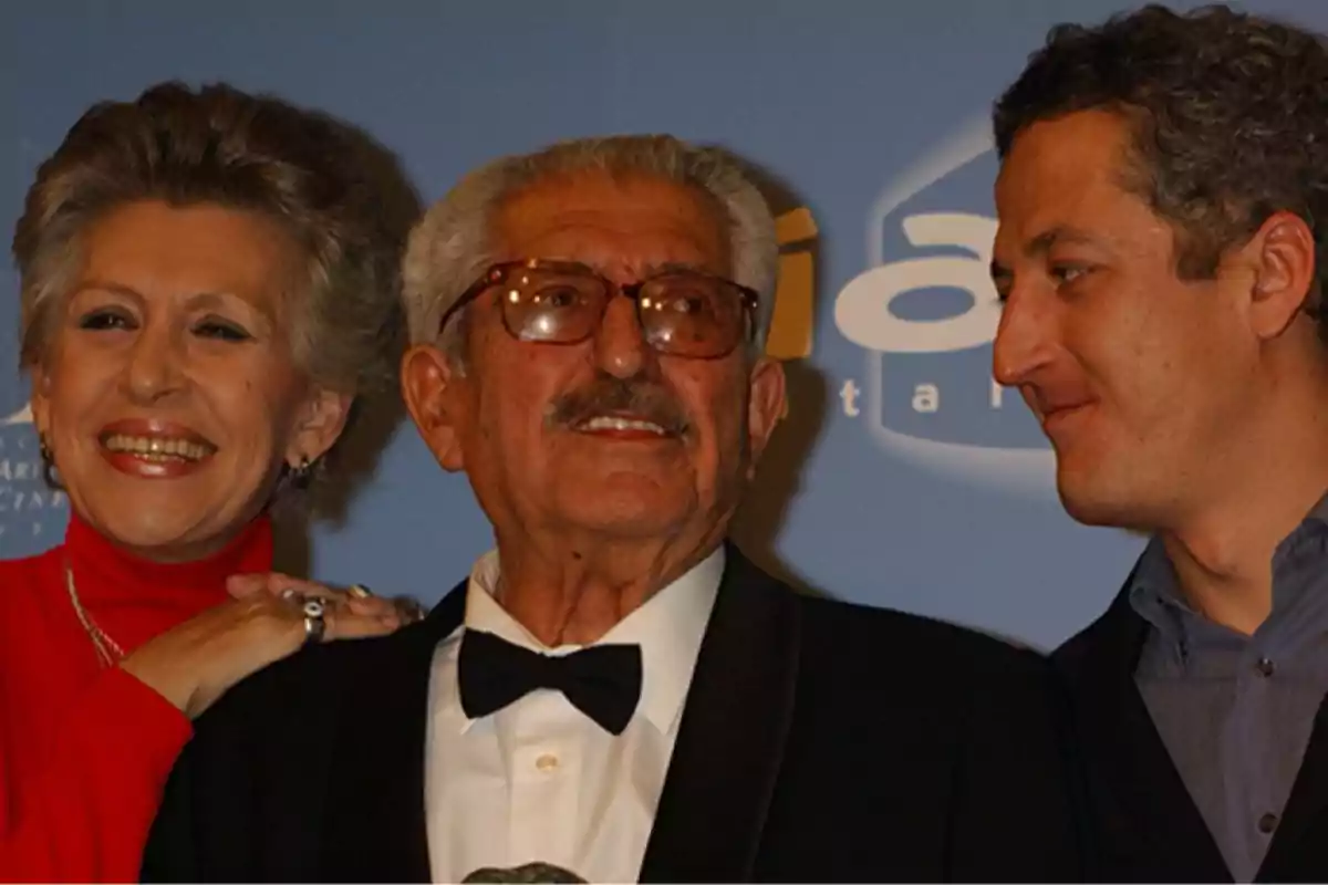 Tres personas sonríen en un evento formal con fondo azul. Tres personas sonríen en un evento formal con fondo azul.