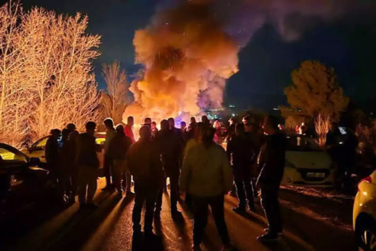 Un grupo de personas se reúne alrededor de un incendio en una carretera durante la noche.
