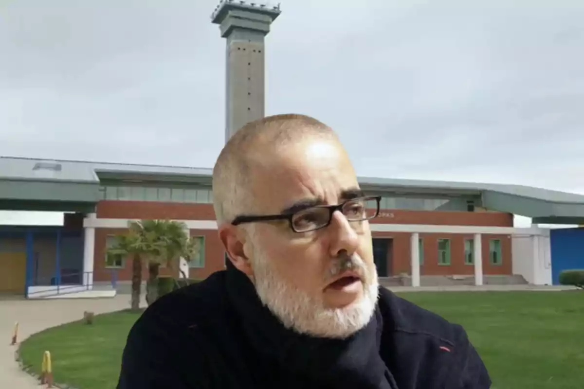 Un hombre con barba y gafas está frente a un edificio con una torre alta en el fondo.