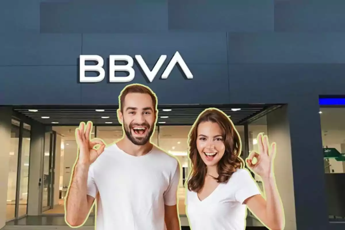 Dos personas sonrientes haciendo el gesto de "OK" frente a una sucursal del banco BBVA.