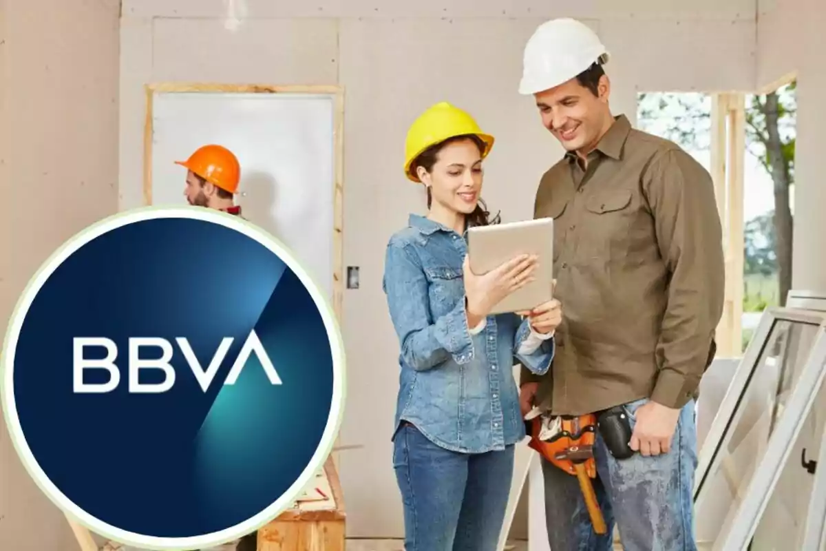 Personas con cascos de construcción revisando una tableta en un sitio de construcción con el logo de BBVA en primer plano.