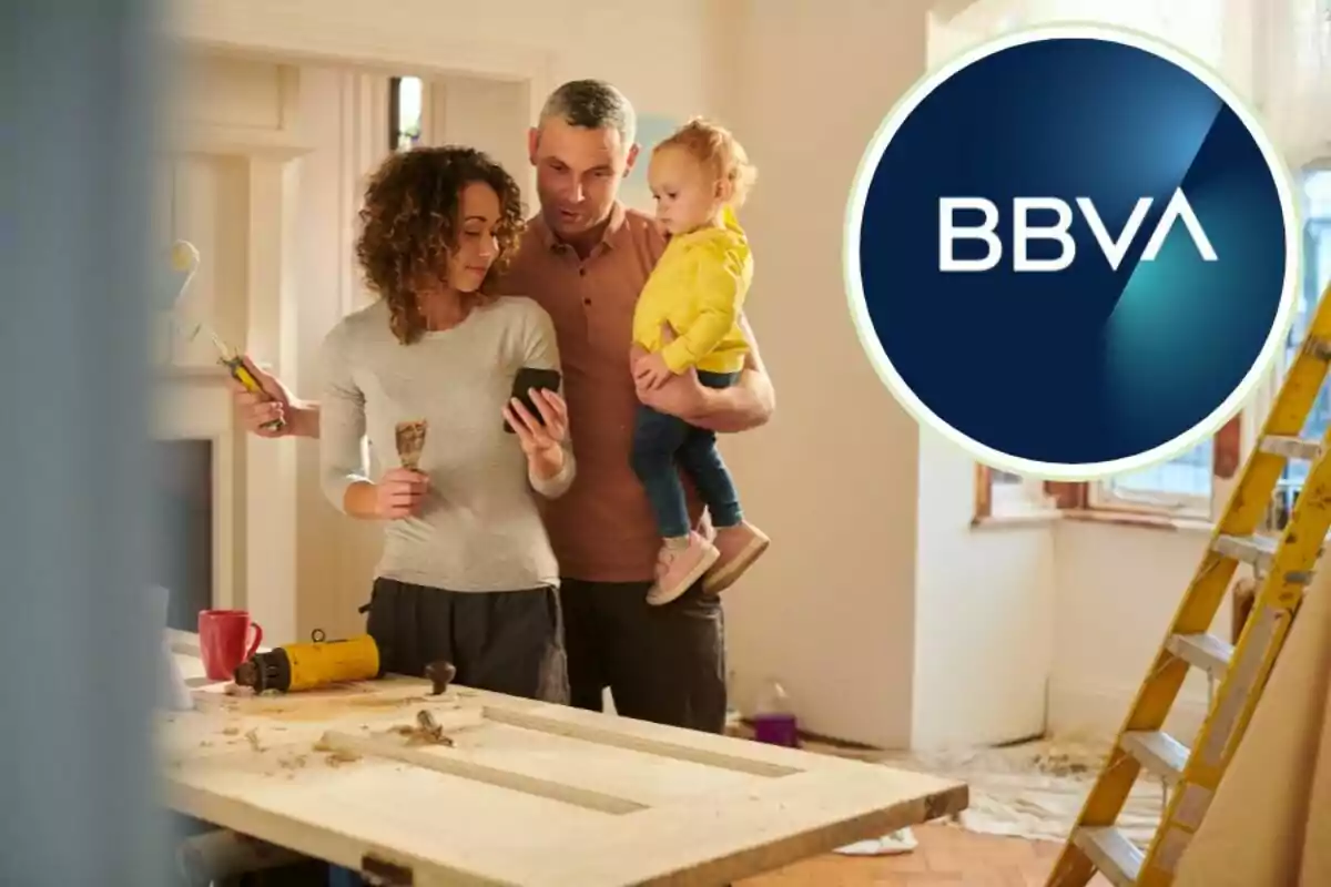 Una familia revisa un teléfono móvil mientras realiza renovaciones en su hogar, con herramientas y una escalera a su alrededor, y el logotipo de BBVA en la esquina superior derecha.