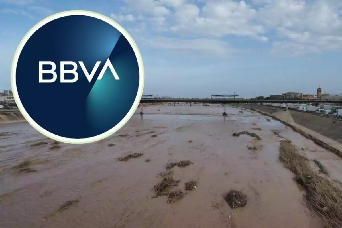 Logotipo de BBVA sobre una imagen de un río desbordado con un puente al fondo y cielo nublado.