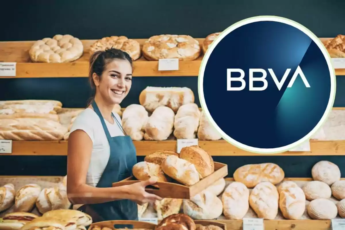 Una mujer sonriente con delantal sostiene una bandeja de pan en una panadería con el logotipo de BBVA superpuesto.