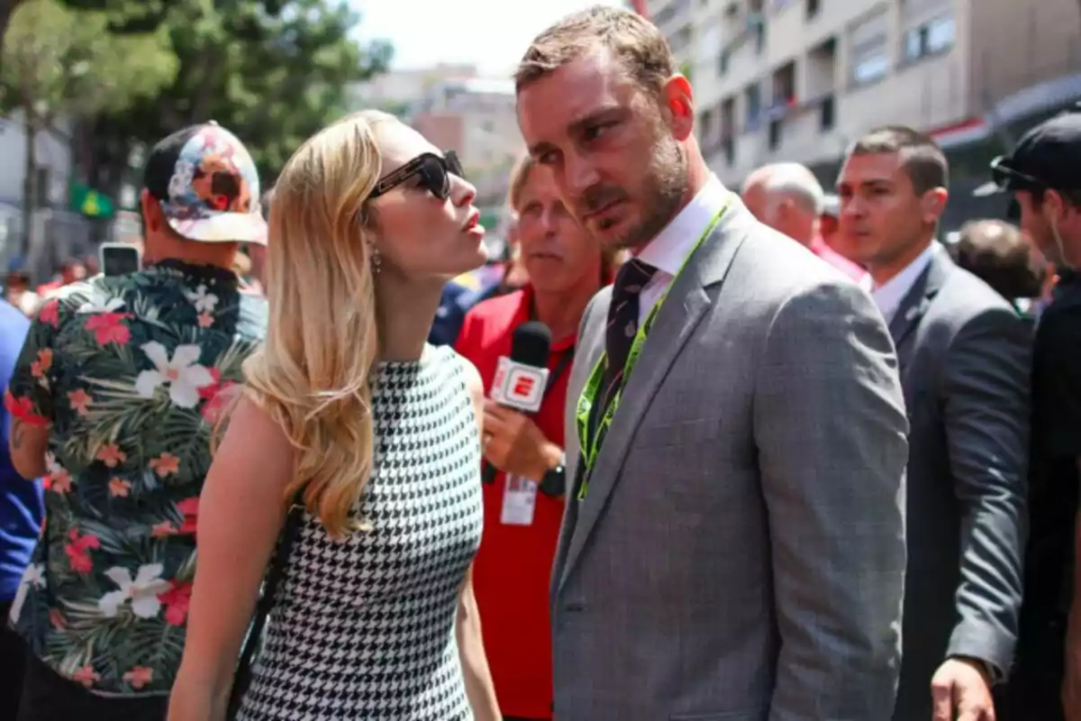 Beatrice Borromeo con gafas de sol y un vestido a cuadros conversa con Pierre Casiraghi de traje en un evento al aire libre, mientras un reportero sostiene un micrófono en el fondo. Beatrice Borromeo con gafas de sol y un vestido a cuadros conversa con Pierre Casiraghi de traje en un evento al aire libre, mientras un reportero sostiene un micrófono en el fondo.