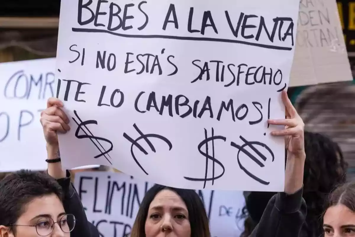 Personas sosteniendo carteles de protesta con mensajes críticos sobre la venta de bebés. Personas sosteniendo carteles de protesta con mensajes críticos sobre la venta de bebés.