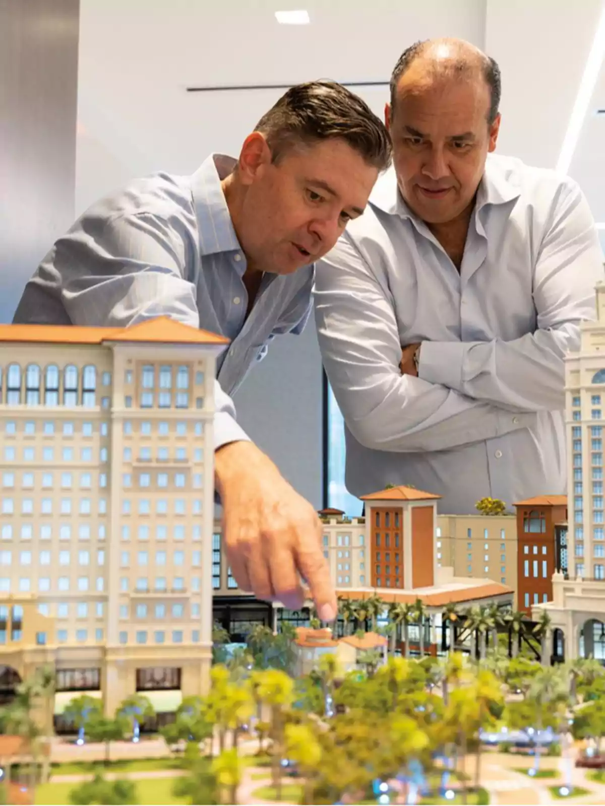 Dos hombres observan y discuten sobre una maqueta arquitectónica detallada de un complejo de edificios.