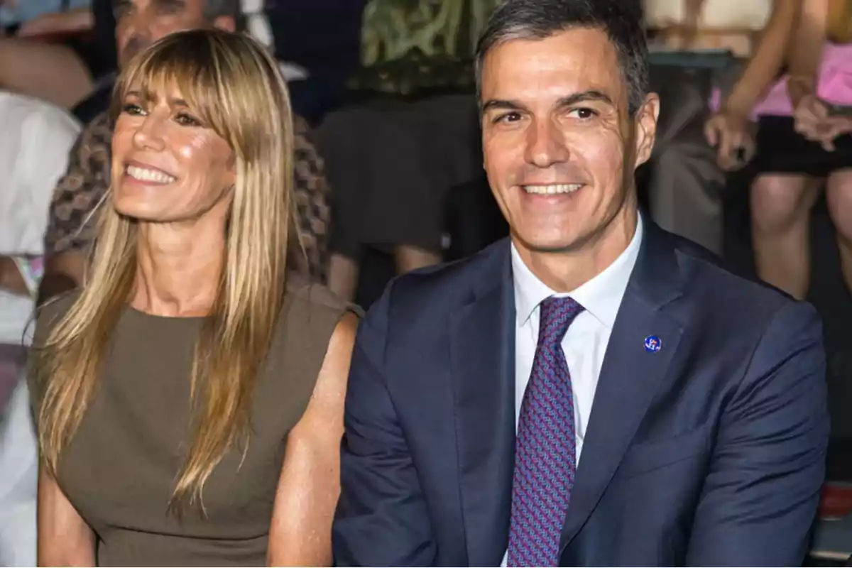 Una pareja sonriente, ella con un vestido sin mangas de color verde oliva y él con un traje azul y corbata roja, sentados en un evento.