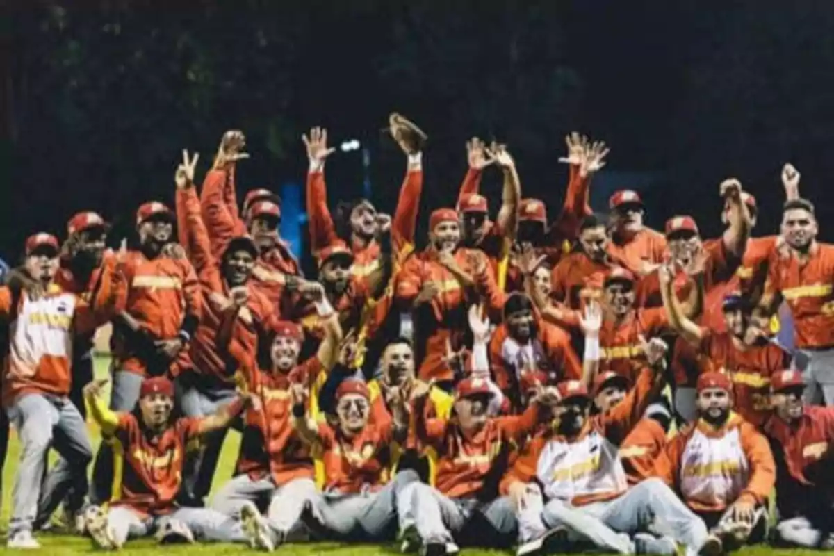 Un equipo de béisbol celebrando en el campo con uniformes rojos y amarillos.