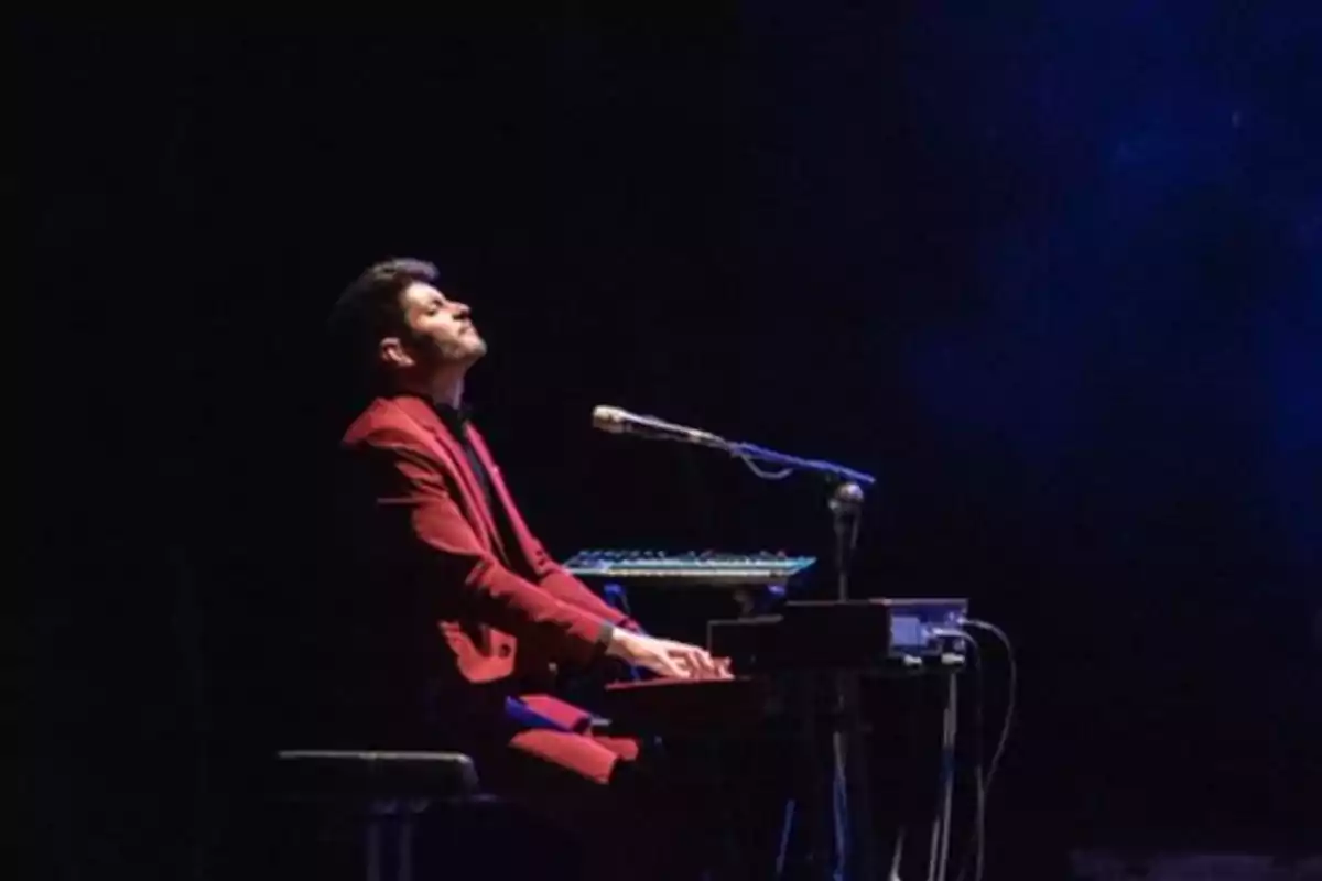 Un hombre tocando el teclado en un escenario oscuro con un traje rojo. Un hombre tocando el teclado en un escenario oscuro con un traje rojo.