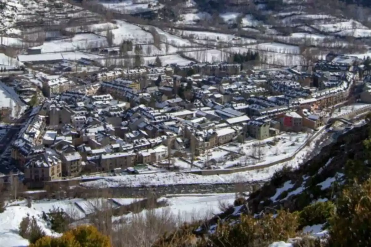 Vista panorámica de un pueblo cubierto de nieve rodeado de montañas y campos nevados.