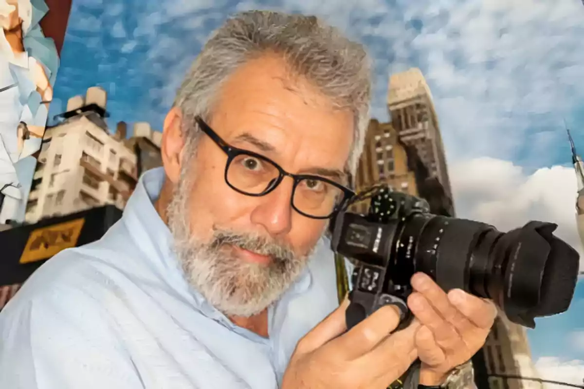 Un hombre con barba y gafas sostiene una cámara en un entorno urbano.