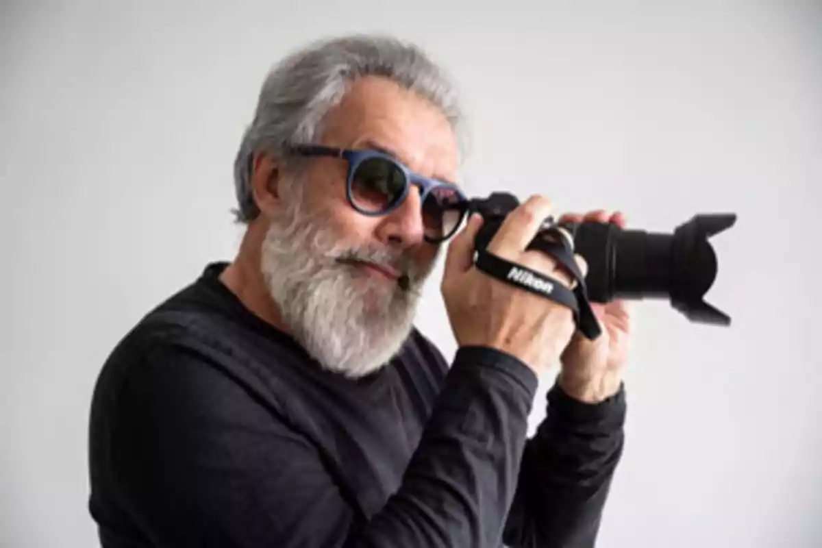 Hombre con barba y gafas de sol sosteniendo una cámara Nikon.