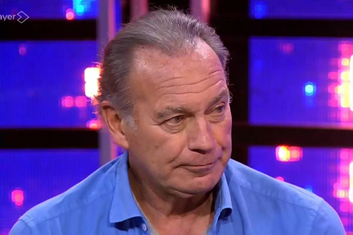 Bertín Osborne mayor con camisa azul en un set de televisión iluminado con luces de colores en Tu Cara Me Suena. Bertín Osborne mayor con camisa azul en un set de televisión iluminado con luces de colores en Tu Cara Me Suena.