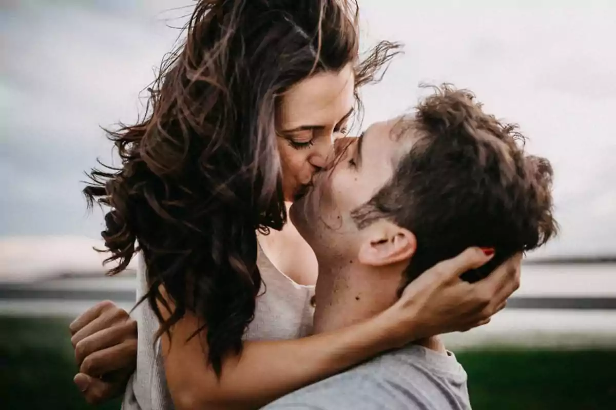 Una pareja besándose apasionadamente al aire libre con el cabello de la mujer ondeando al viento.