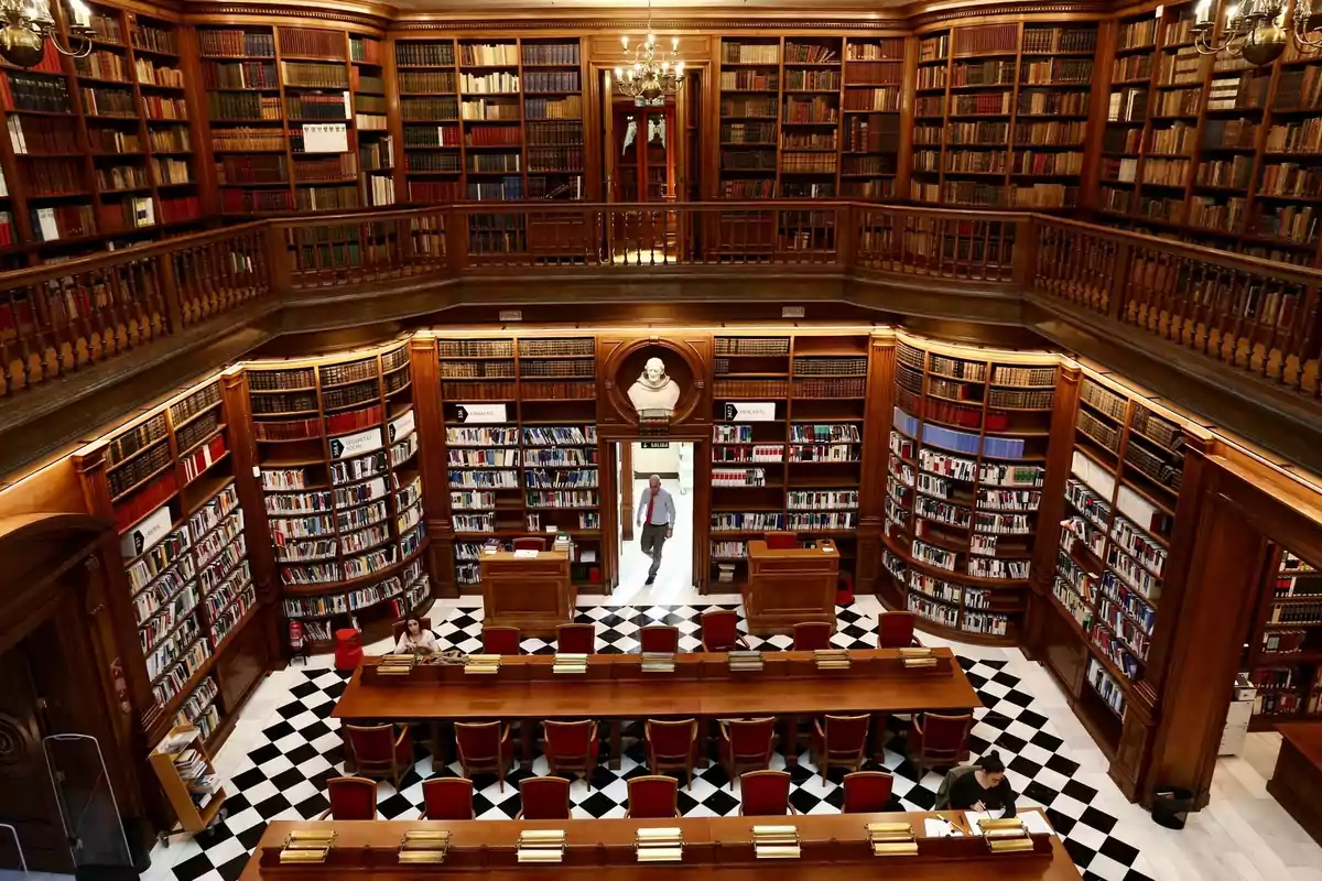 Una biblioteca antigua con estanterías de madera llenas de libros y mesas de lectura con sillas rojas.