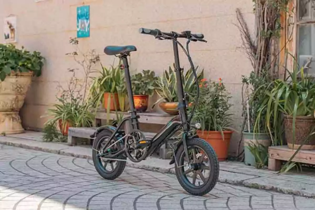 Bicicleta plegable negra estacionada en un patio con macetas y plantas alrededor.