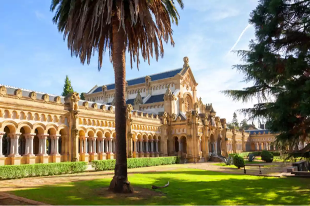 Edificio histórico con arcos y columnas rodeado de jardines y palmeras bajo un cielo azul.