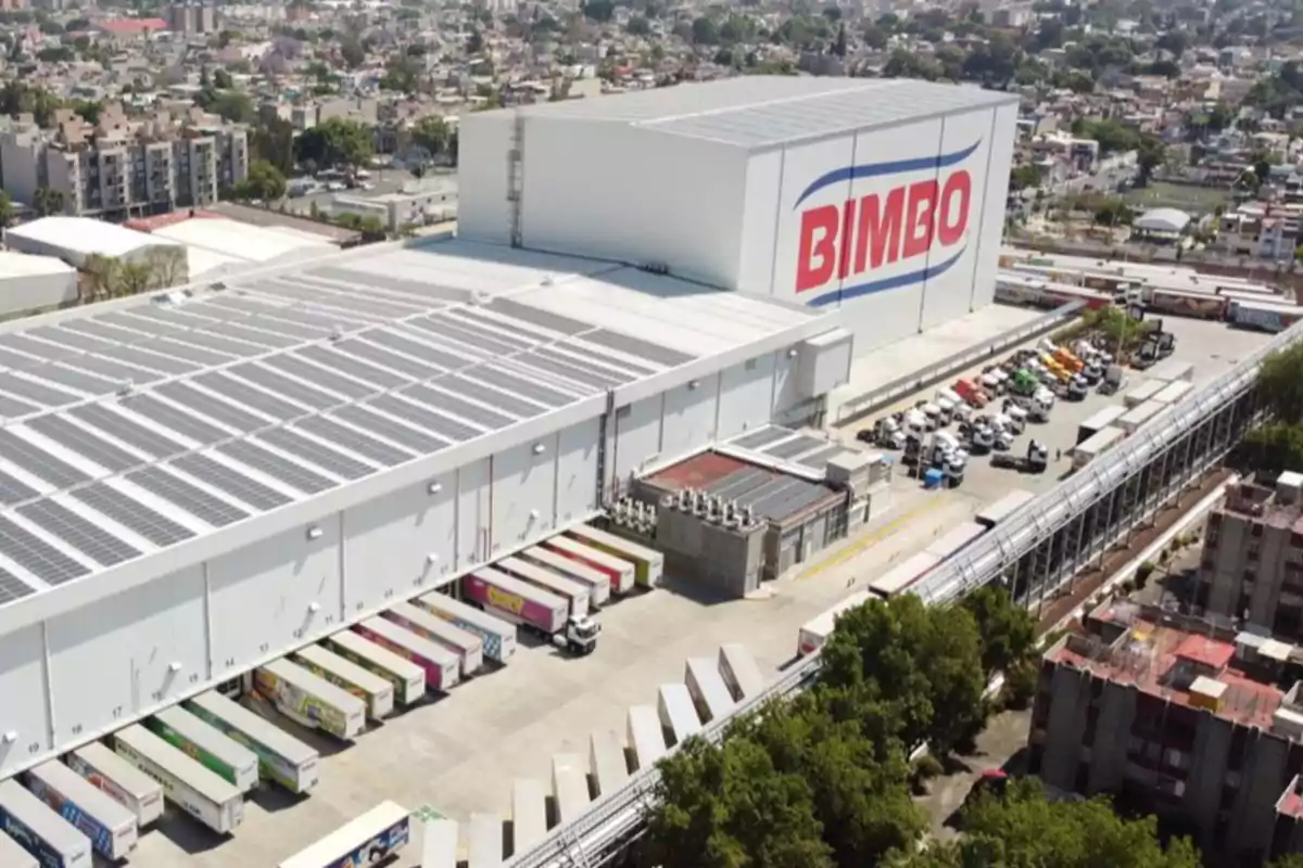 Vista aérea de una planta industrial con paneles solares en el techo y varios camiones estacionados en el área de carga. Vista aérea de una planta industrial con paneles solares en el techo y varios camiones estacionados en el área de carga.