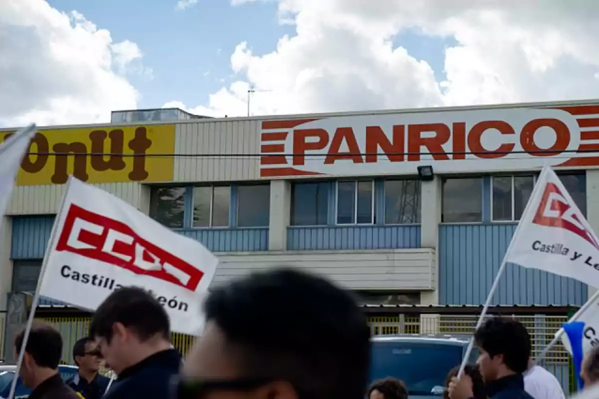 Personas con banderas de un sindicato protestan frente a un edificio con los logotipos de Donut y Panrico.